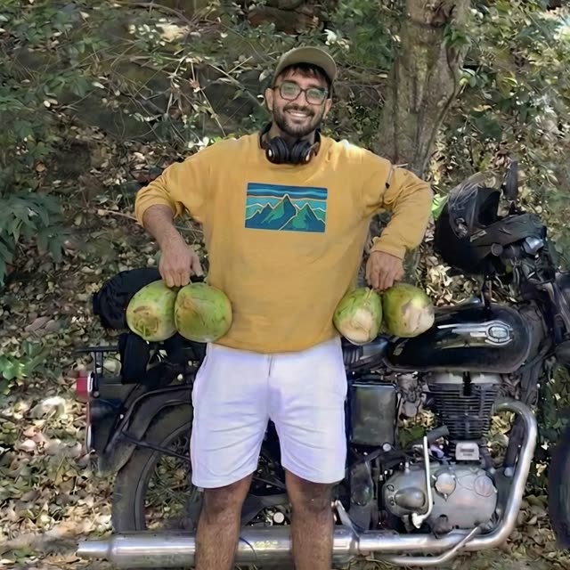 Digvijay Shekhawat on a forest road, holding four coconuts, motorcycle behind him